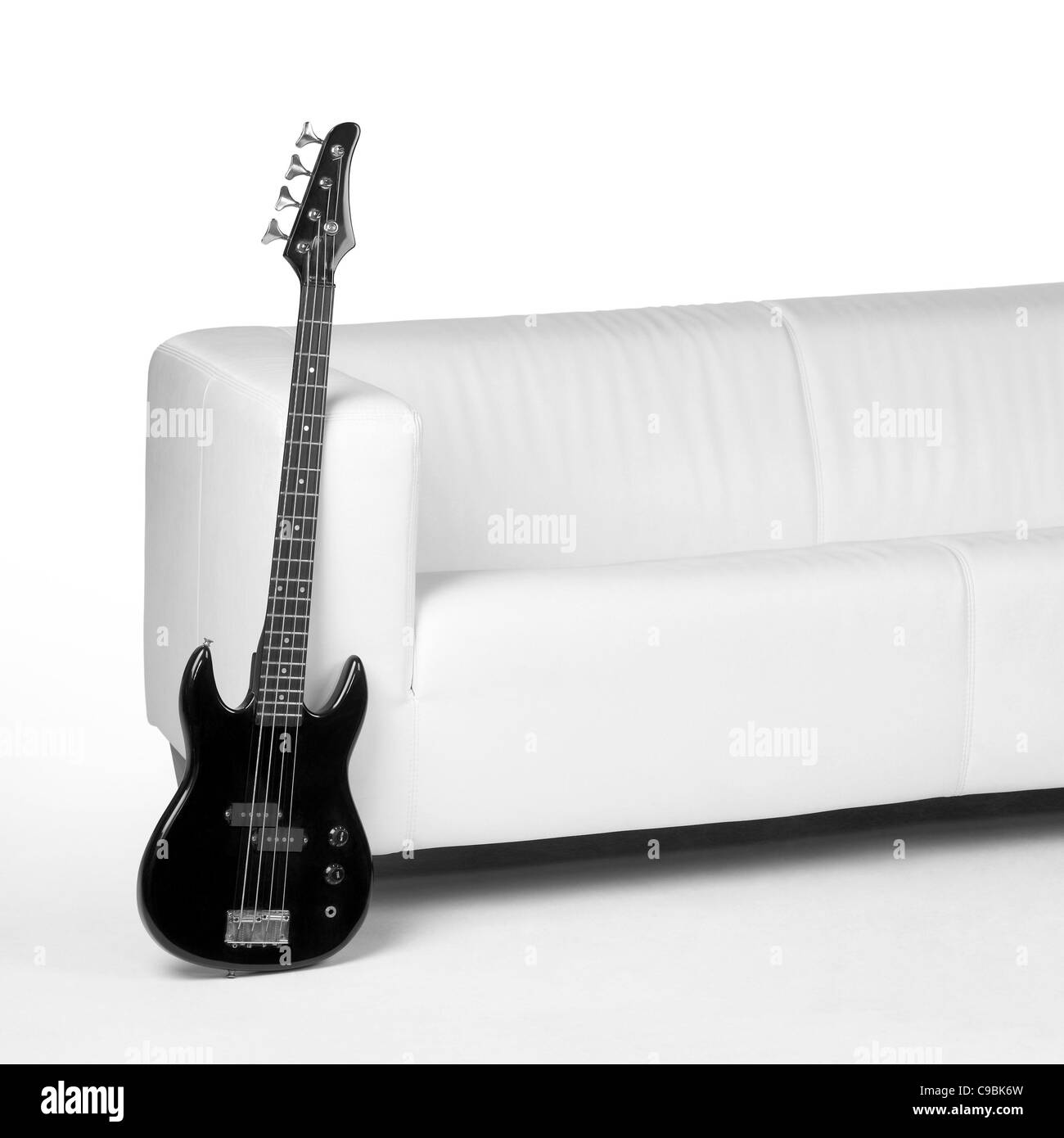 Black Bassgitarre an weißen Couch in weißem Rücken lehnen Stockfoto