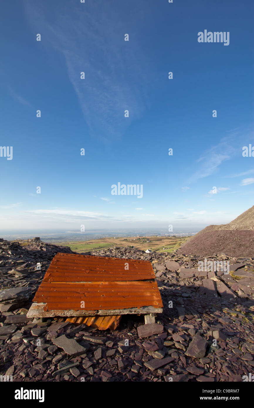 Rostige Wellblech Trümmer auf einen stillgelegten Schieferbergwerk Tipp, Snowdonia, Blick nach unten auf die Menai Straits in der Ferne. Stockfoto