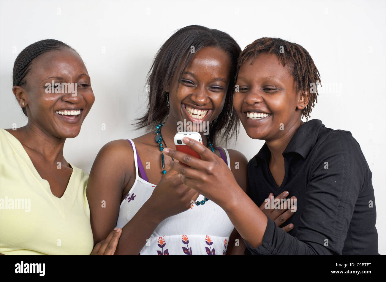 Drei junge kenianische Frauen genießen Sie eine Nachricht an einem Telefon, Nairobi, Kenia Stockfoto