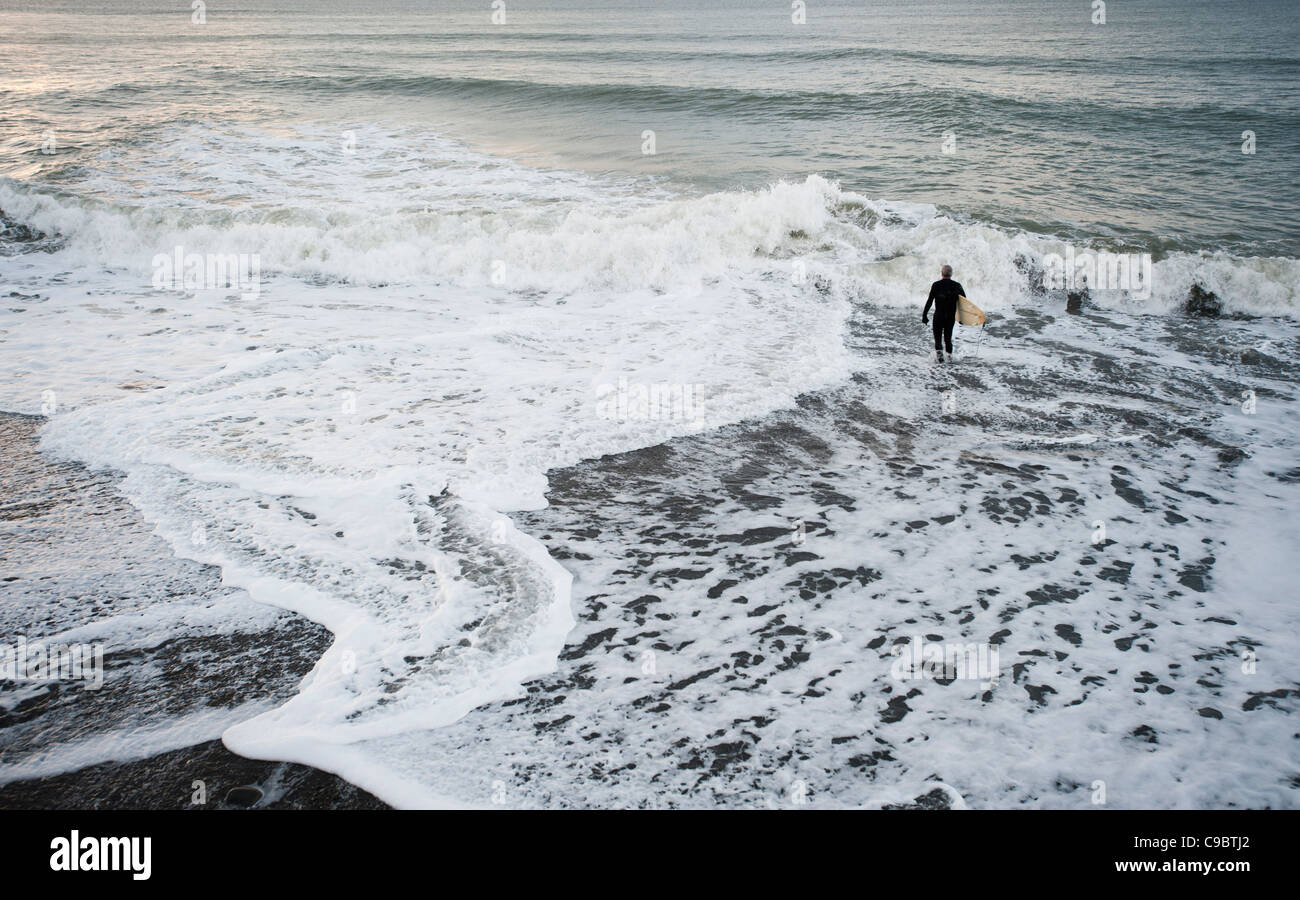 Ein Mann zu gehen Surfen im Meer, Cardigan Bay, Aberystwyth, November, Wales UK Stockfoto