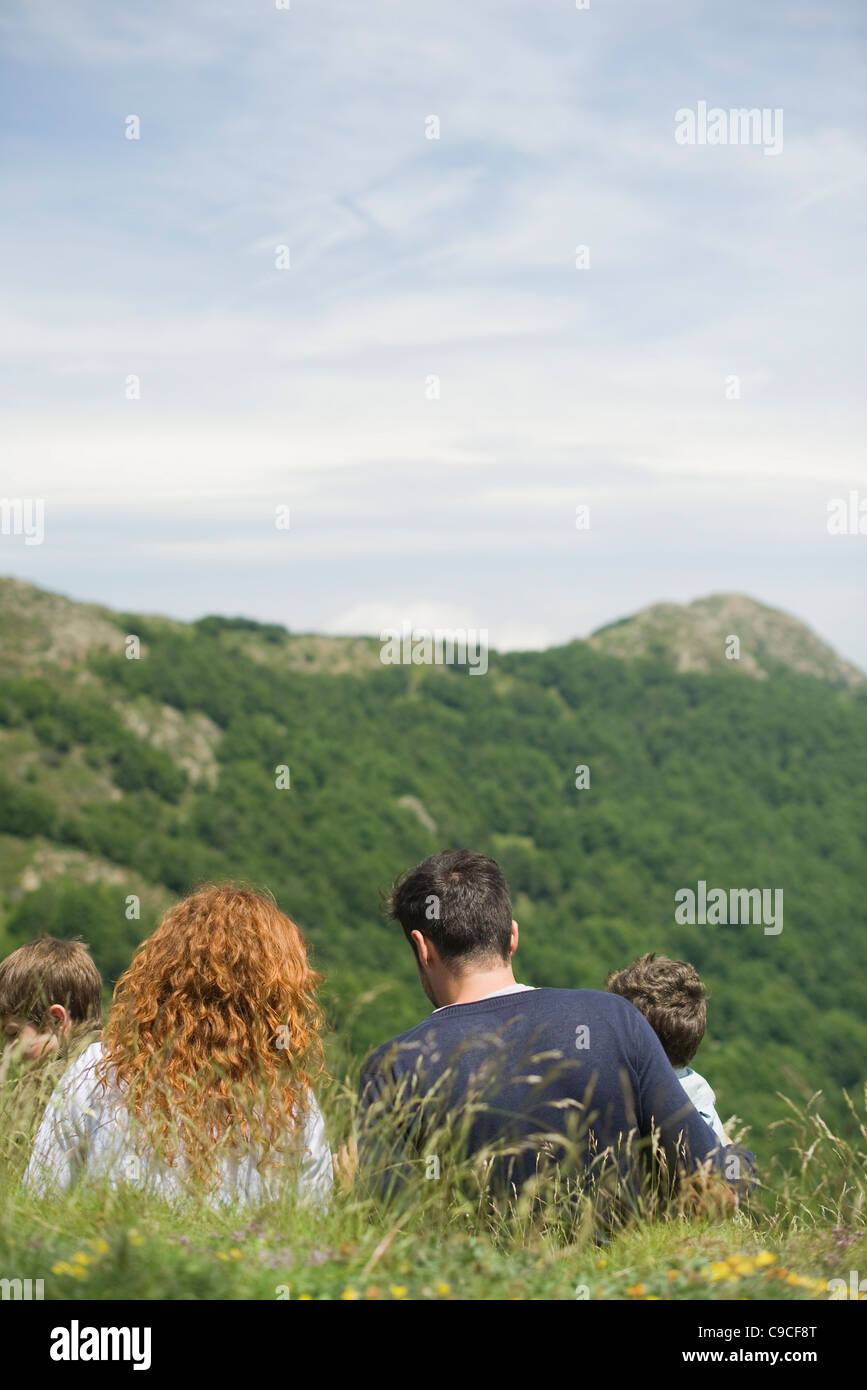Eltern und Kinder sitzen auf der Wiese Blick auf Berge, Rückansicht Stockfoto