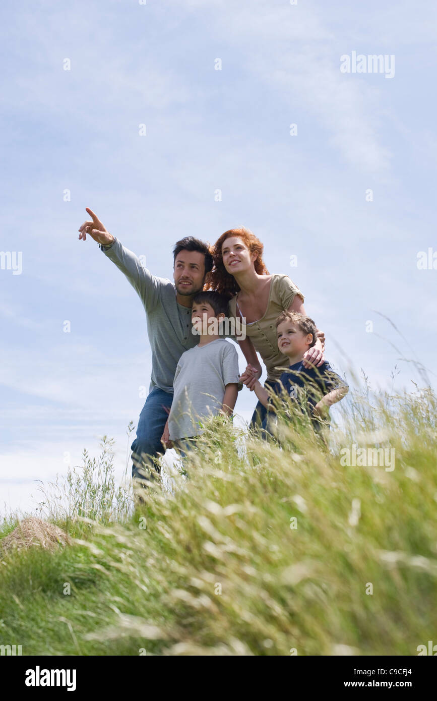 Eltern und zwei Jungs stehen auf Wiese, Vater zeigt in Ferne Stockfoto