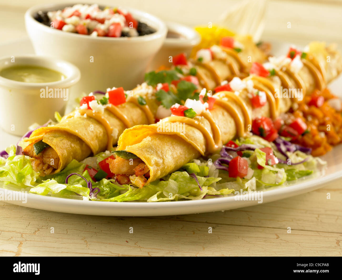 Zwei Hühner Taquitos garniert mit Sauce, Salsa und Käse und serviert ...