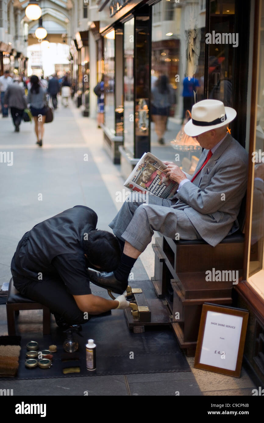 Ein Mann hat seine Schuhe glänzte, während er einer Zeitung in die Burlington Arcade eine teure Einkaufspassage liest. London, UK Stockfoto