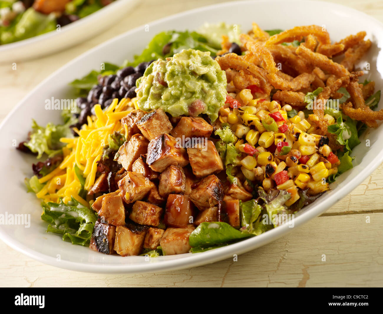 Grill-Hähnchen-Salat mit Kopfsalat, Mais, schwarze Bohnen, Käse, Zwiebelringe und Guacamole gehackt Stockfoto