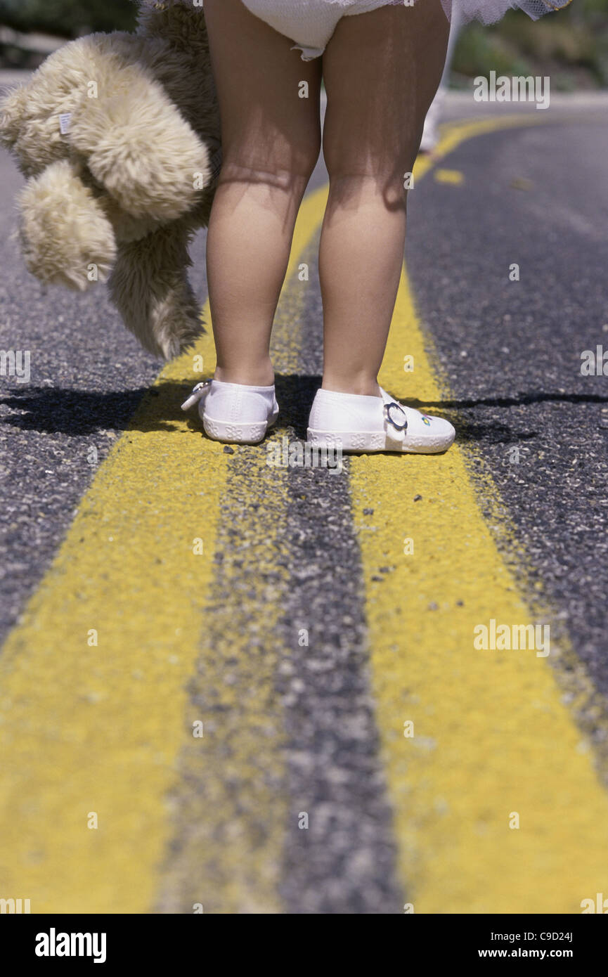 Niedrige Schnittansicht eines Mädchens Füße stehen auf einer Straße hält ein Stofftier Stockfoto