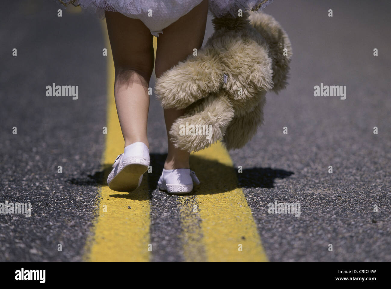 Niedrige Schnittansicht eines Mädchens Füße zu Fuß auf einer Straße hält ein Stofftier Stockfoto