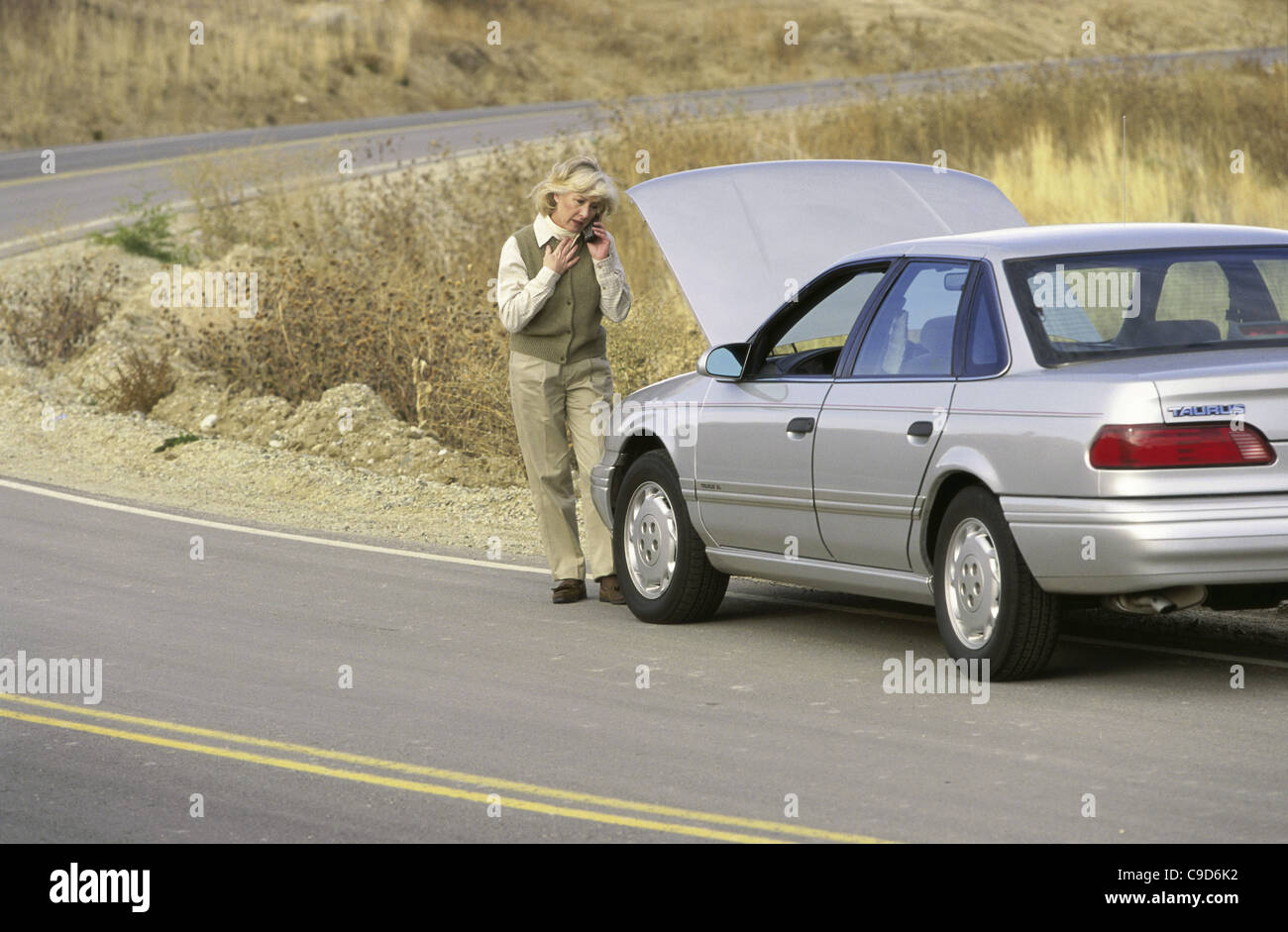 Ältere Frau stand vor eine kaputte Auto telefonieren mit einem Handy Stockfoto