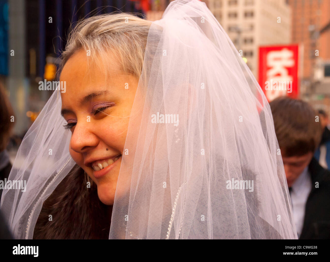 Manhattan, New York, USA: Lächelnd Braut setzt auf ihren Mantel nach posiert, mit ihrem Bräutigam und Hochzeitsgesellschaft für Hochzeitsfotos im Freien auf dem Times Square, New York, auf Dienstag, 24. Januar 2012, nach der Trauung Rathaus. Die Temperaturen waren ungewöhnlich warm, bis 52° C / 11° C am Nachmittag. Stockfoto