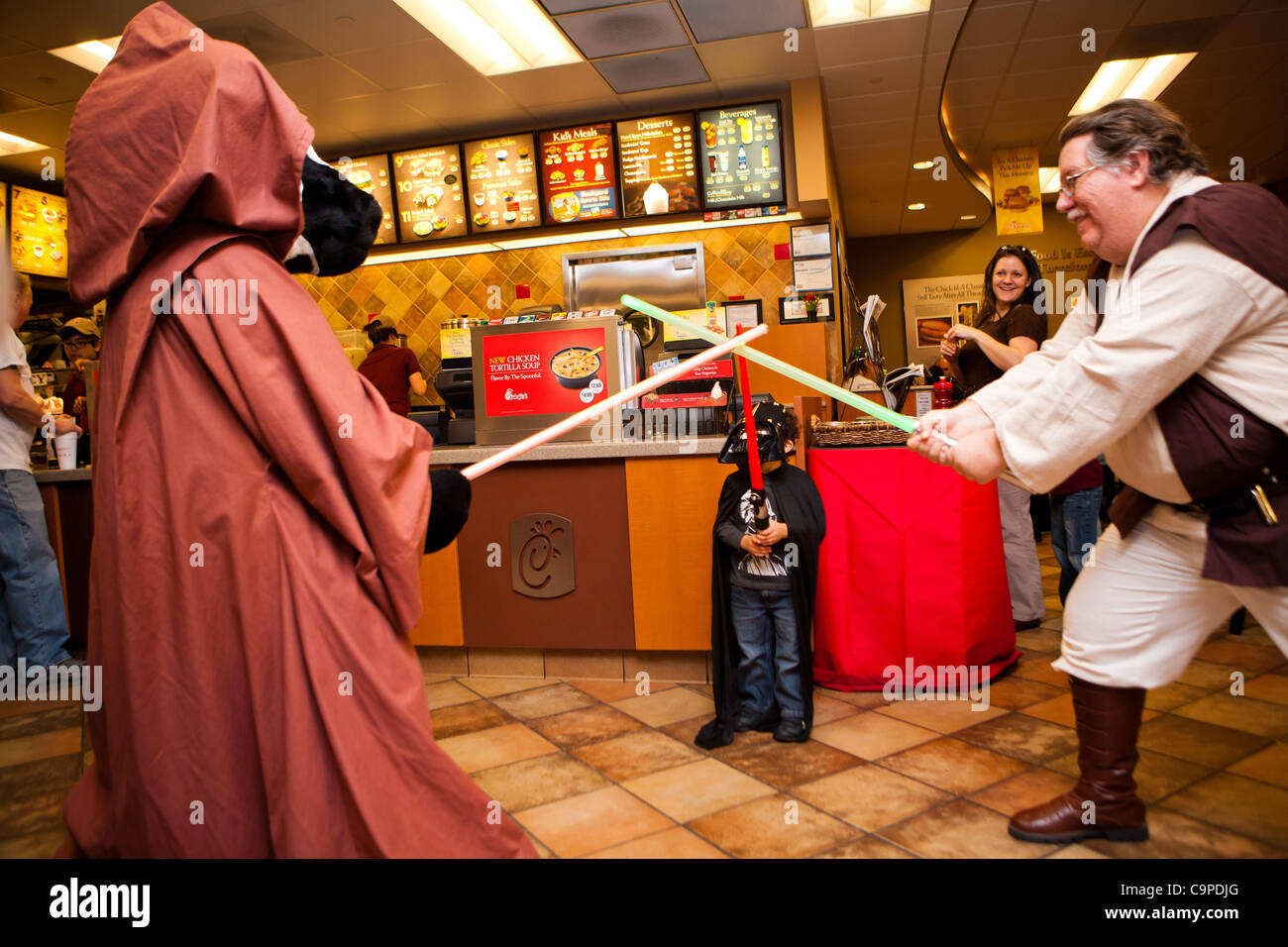 7. Februar 2012 - Houston, Texas, USA - A junge Star Wars Fan in einem Darth Vader Kostüm mit seinen Lichtschwertern kämpfen mit der Chick-Fil-A Cow und Obi Wan Kenobi. Chick-Fil-A Mitarbeiter in Houston, Texas Star Wars Kostüme tragen, die Veröffentlichung von Star Wars Episode 1 - The Phantom Menace 3D zu fördern. ( Stockfoto