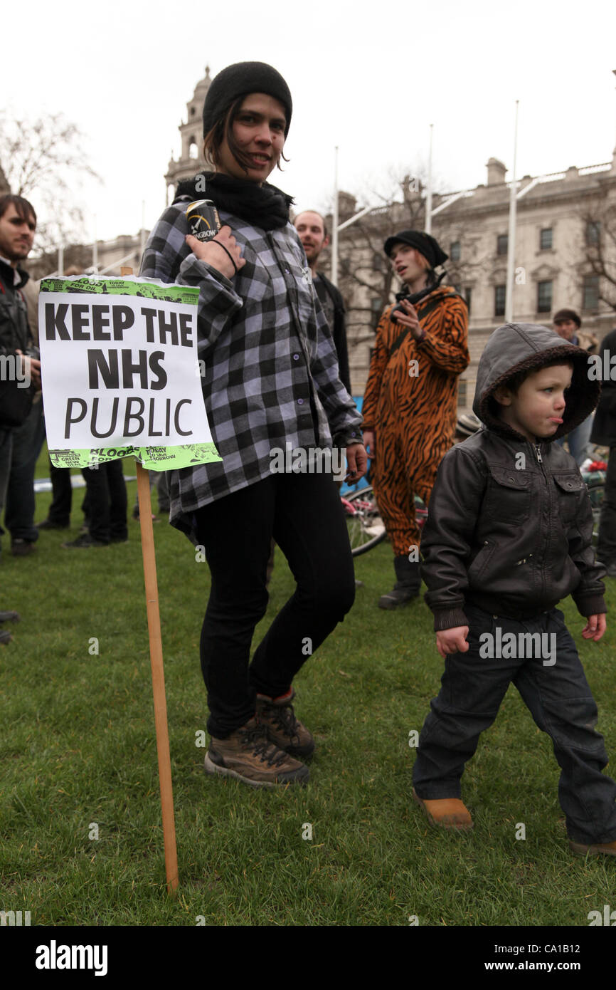 London, UK. 18. März 2012. Mitglied der OccupyLondon spielt mit einem kleinen Kind auf dem Grün des Parliament Square. Das Plakat von einem vorherigen Protest von der Save zurückgelassen wurde unsere Nhs-Gruppe. Es gab etwa 40 Personen, die auf den Platz halten die Occupy-Banner und ein sound-System mit Musik pl Stockfoto