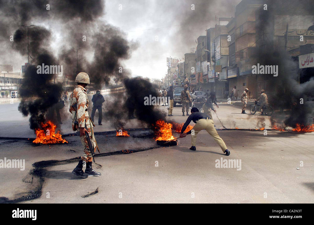 Polizisten nehmen Sie brennende Reifen, die an der Liaquatabad Road in Flammen vom wütenden Mob festgelegt wurden, wie Gewalt in der Stadt nach der Tötung eines Aktivisten der Muttehda Qaumi Bewegung (MQM), Mansoor Mukhtar und sein Bruder Masood Mukhtar in Karachi auf Dienstag, 27. März 2012 ausbricht. Stockfoto