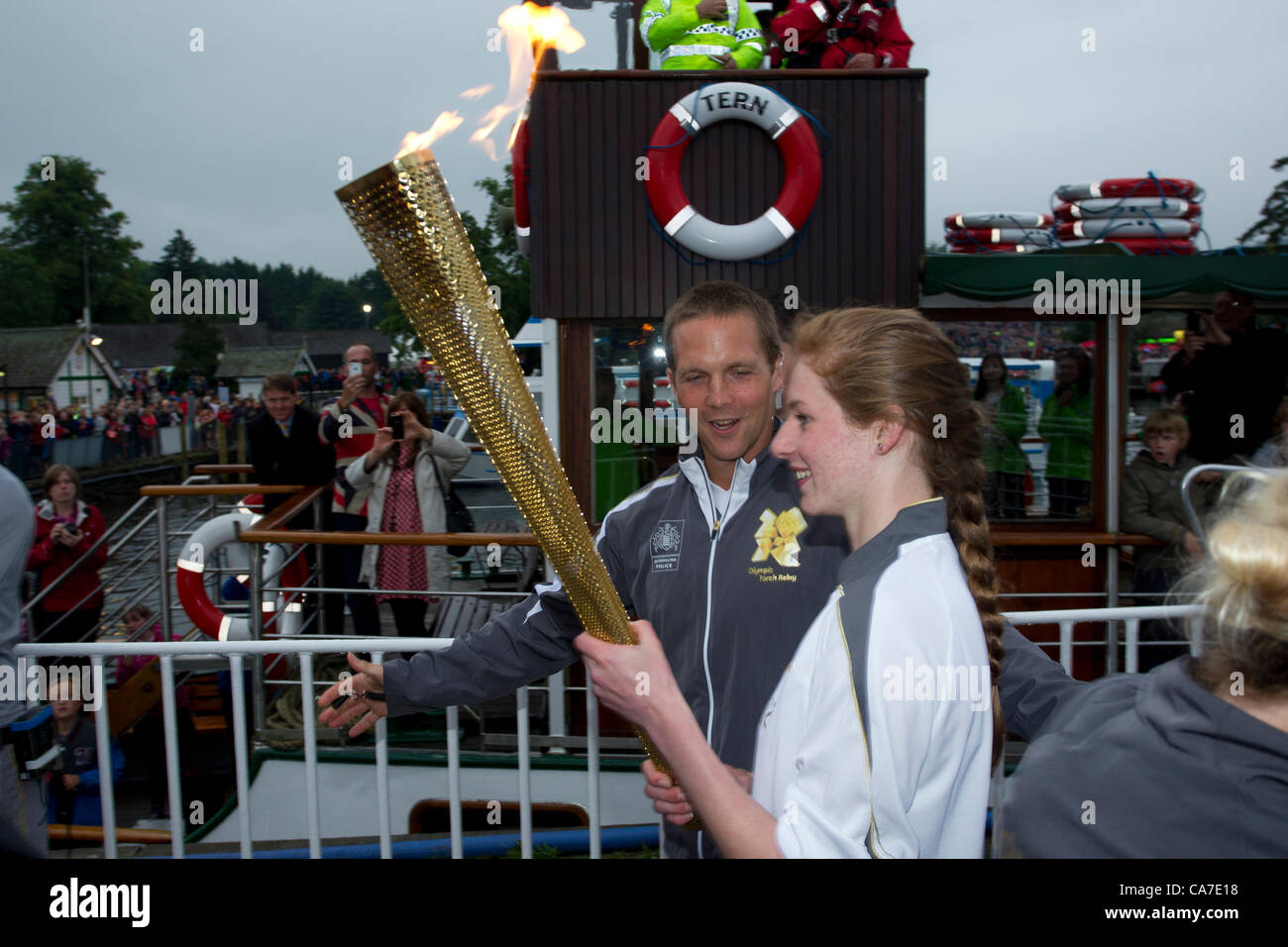 Stephanie Booth mit Olympischen Fackel auf dem Dampf Cruiser The Tern bei der Ankunft in Bowness auf Windermere er Olympische Feuer an der historischen Dampfschiff Tern an Waterhead Pier Bord bereisen zu Bowness auf Windermere.In eines der größten Spektakel, die jemals in den Lake District, die Flamme der See von hundert andere Schiffe eskortiert überquert. Die Hauptaufgabe der Fackel-Sicherheitsteam Läufer - hier in grau - gesehen ist die Kontinuität der Flamme zu schützen und so zum Schutz der Fackel und Fackelträger TST Olympischer Fackellauf Stockfoto