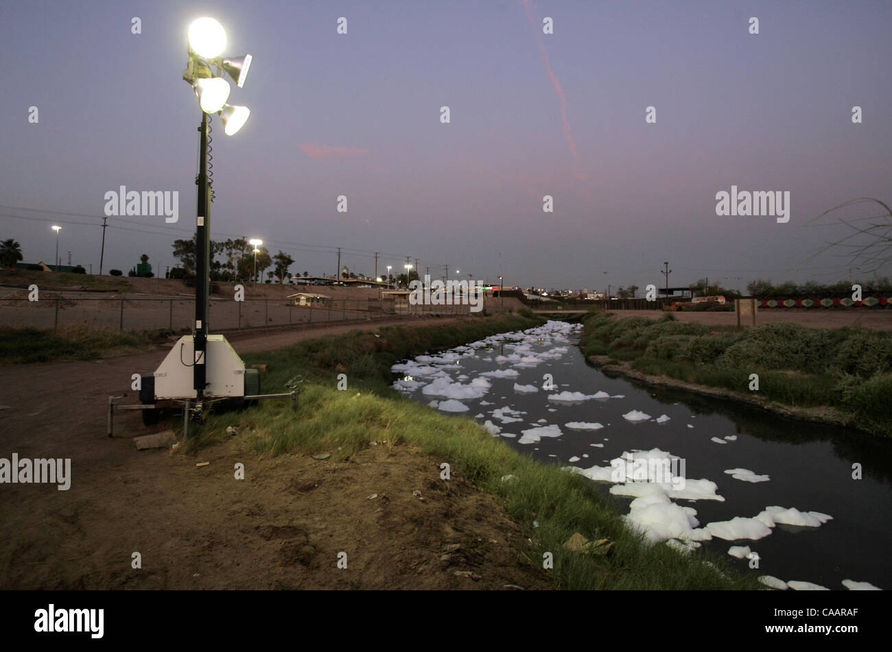 Klumpen von Schaum Schwimmer Nord in Calexico aus Mexicali, Mexiko in der Abenddämmerung in hoch belasteten New River in der Nähe des Grenzübergangs. Generator angetrieben Flutlichter platziert es durch die Border Patrol beleuchten in diesem Abschnitt, die oft von Menschen mit dem Fluss zu illegal ins Land schweben verwendet wird.  U/T Stockfoto