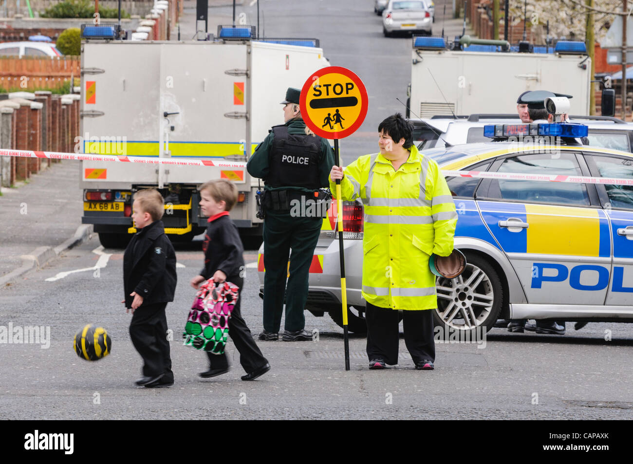 Kinder überqueren Sie die Straße an einem bemannten Fußgängerüberweg während eine Sicherheitswarnung mit Bomb Squad in Belfast, im Hintergrund zeigt, dass das Leben immer noch trägt auf. Stockfoto