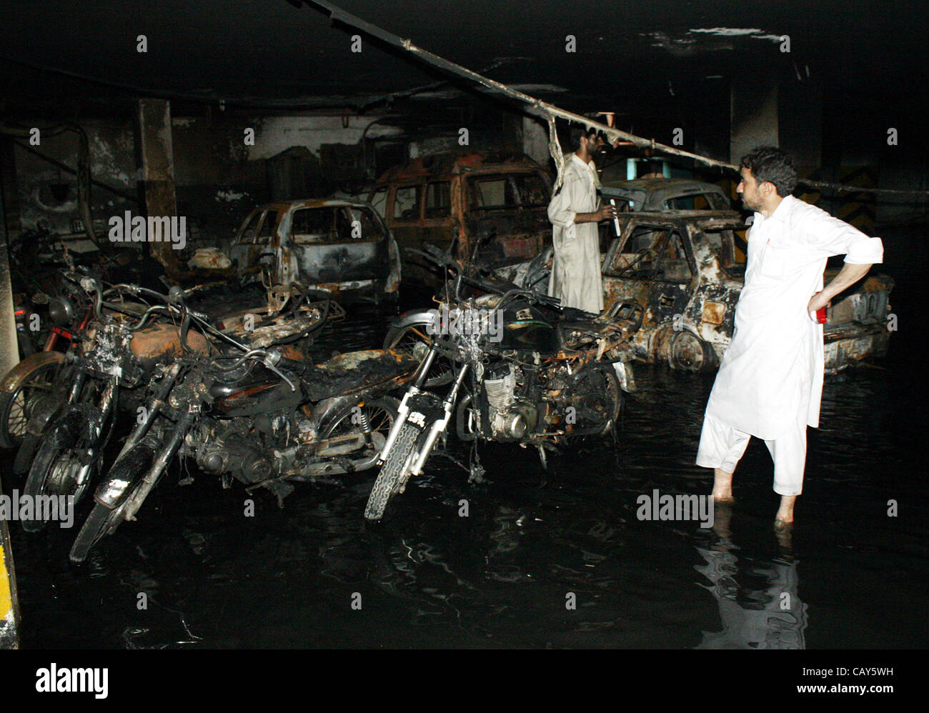Die Menschen schauen verbrannten Fahrzeuge und Motorräder, die aus unbekannten Gründen brannte wurden nach dem Feuer Vorfall im Keller des West-Land-Apartment im Bahadurabad Bereich am frühen Morgen in Karachi auf Montag, 7. Mai 2012 ausbrach. Stockfoto