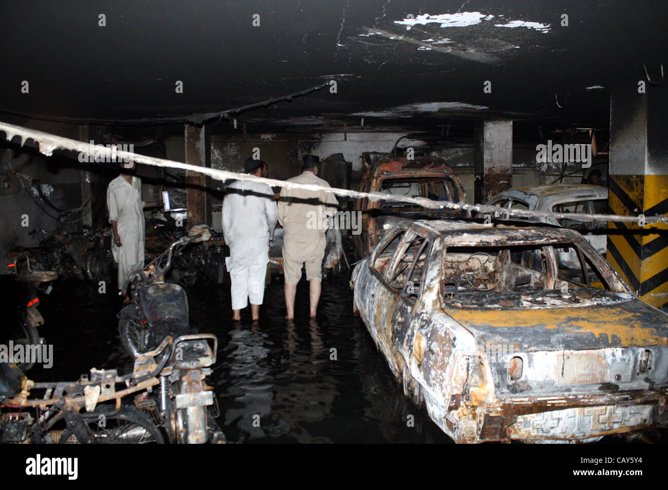 Die Menschen schauen verbrannten Fahrzeuge und Motorräder, die aus unbekannten Gründen brannte wurden nach dem Feuer Vorfall im Keller des West-Land-Apartment im Bahadurabad Bereich am frühen Morgen in Karachi auf Montag, 7. Mai 2012 ausbrach. Stockfoto