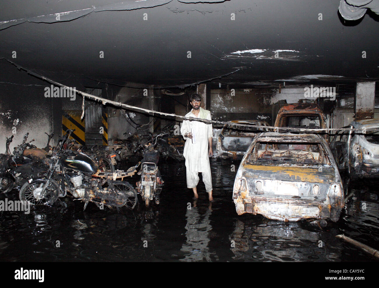 Ein Mann steht in der Nähe von verbrannten Fahrzeuge und Motorräder, die aus unbekannten Gründen brannte wurden nach dem Feuer Vorfall im Keller des West-Land-Apartment im Bahadurabad Bereich am frühen Morgen in Karachi auf Montag, 7. Mai 2012 ausbrach. Stockfoto
