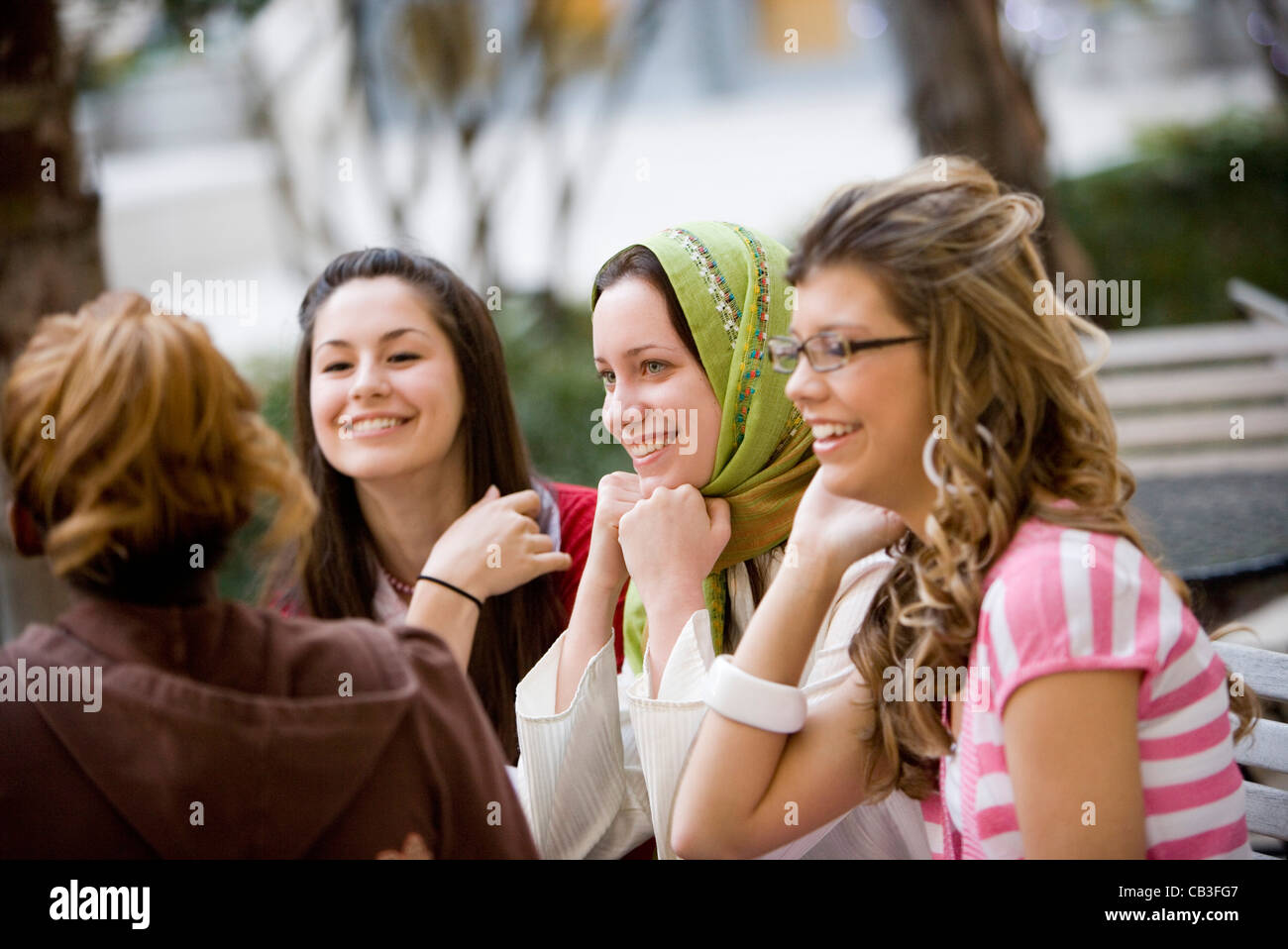 Ansicht von vier jungen Frauen im Gespräch beim Sitzen am Tisch im Garten Stockfoto