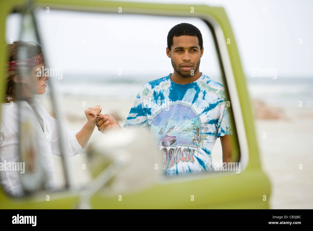 Junger Mann und junge Frau, die mit einem Fahrzeug am Strand Stockfoto