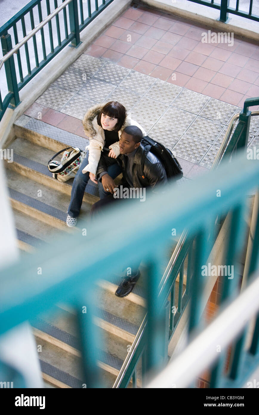 Inter-racial Pärchen sitzt am unteren Ende der Treppe an einem öffentlichen Bahnhof Stockfoto