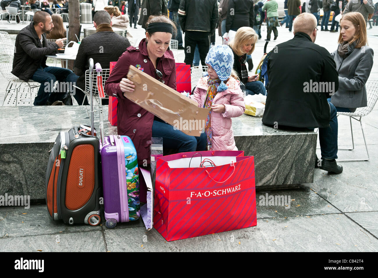 touristischen Mutter & kleine Tochter mit Weihnachts-shopping Einkäufe im FAO Schwartz Einkaufstasche auf der Plaza vor Shop Eingang Stockfoto