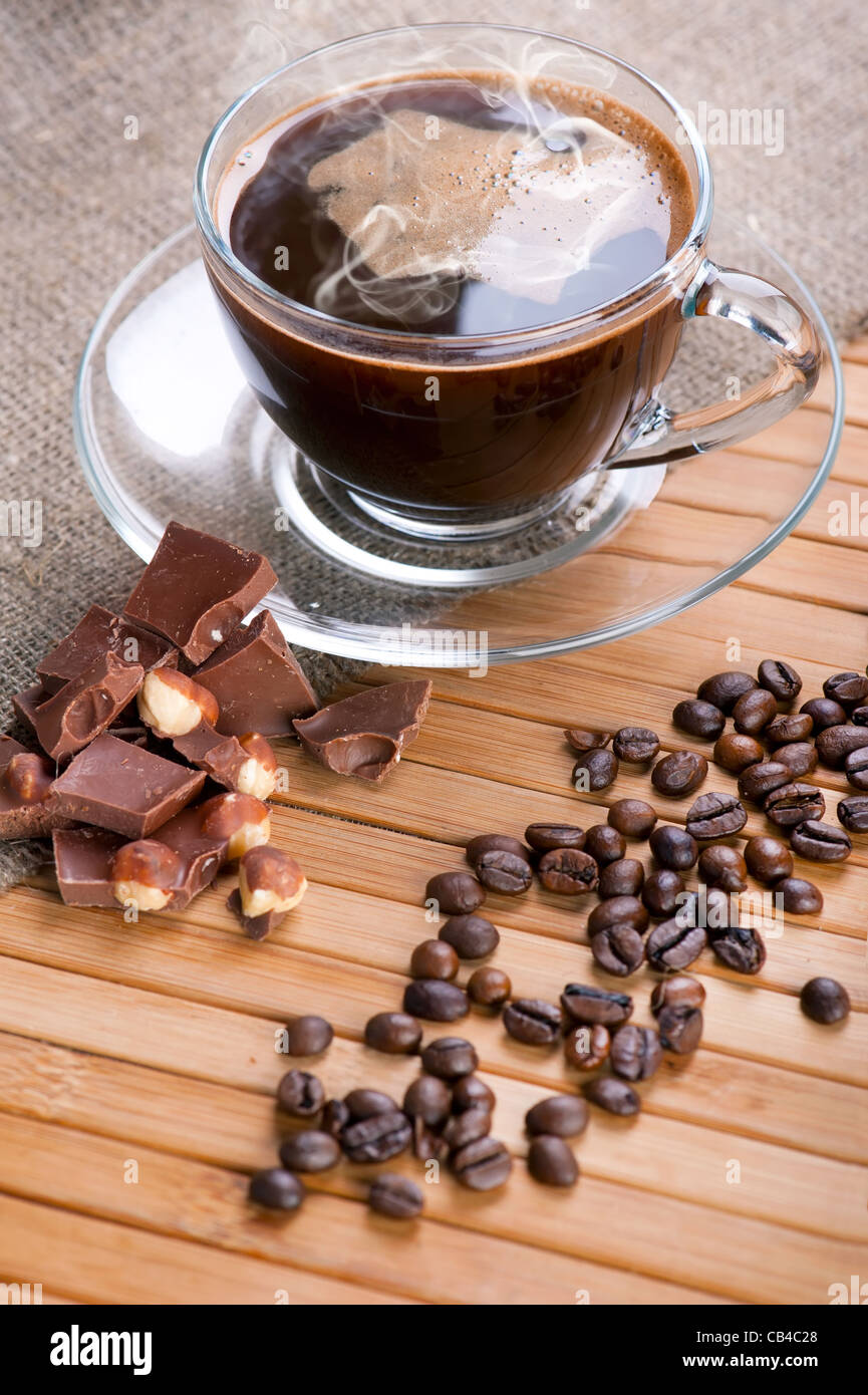 Tasse Kaffee, Schokolade mit Nüssen und Kaffeebohnen auf hölzernen Hintergrund mit Leinwand Stockfoto