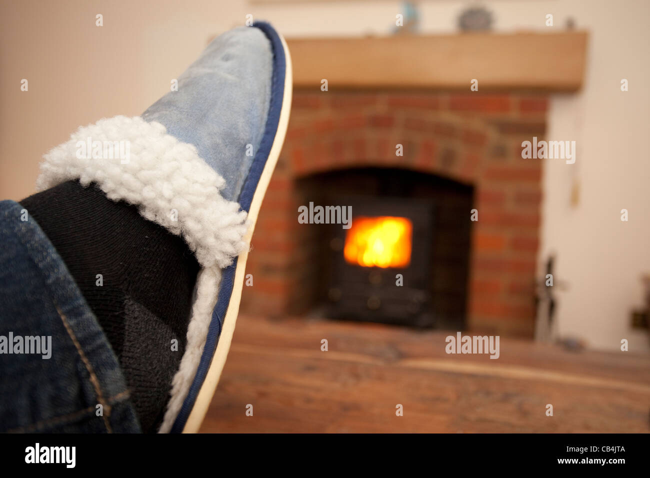 Füße hoch auf Tisch mit Log brennenden Ofen im Hintergrund Stockfoto