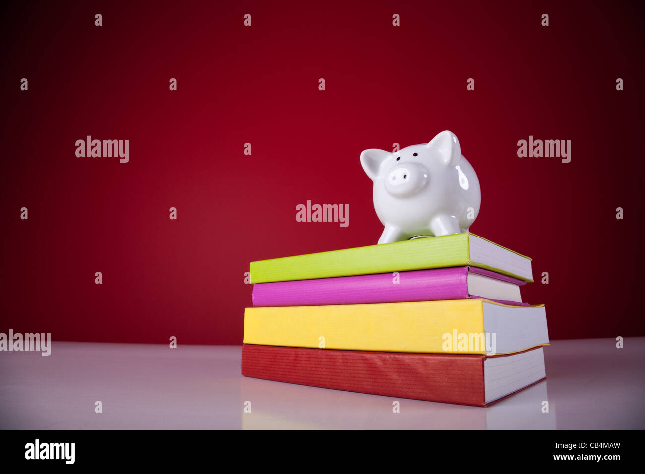 Piggy Bank über einen Stapel bunten Bücher mit einem roten Hintergrund Stockfoto