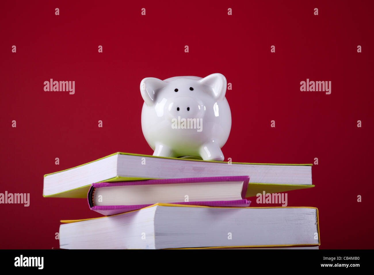 Piggy Bank über einen Stapel bunten Bücher mit einem roten Hintergrund Stockfoto