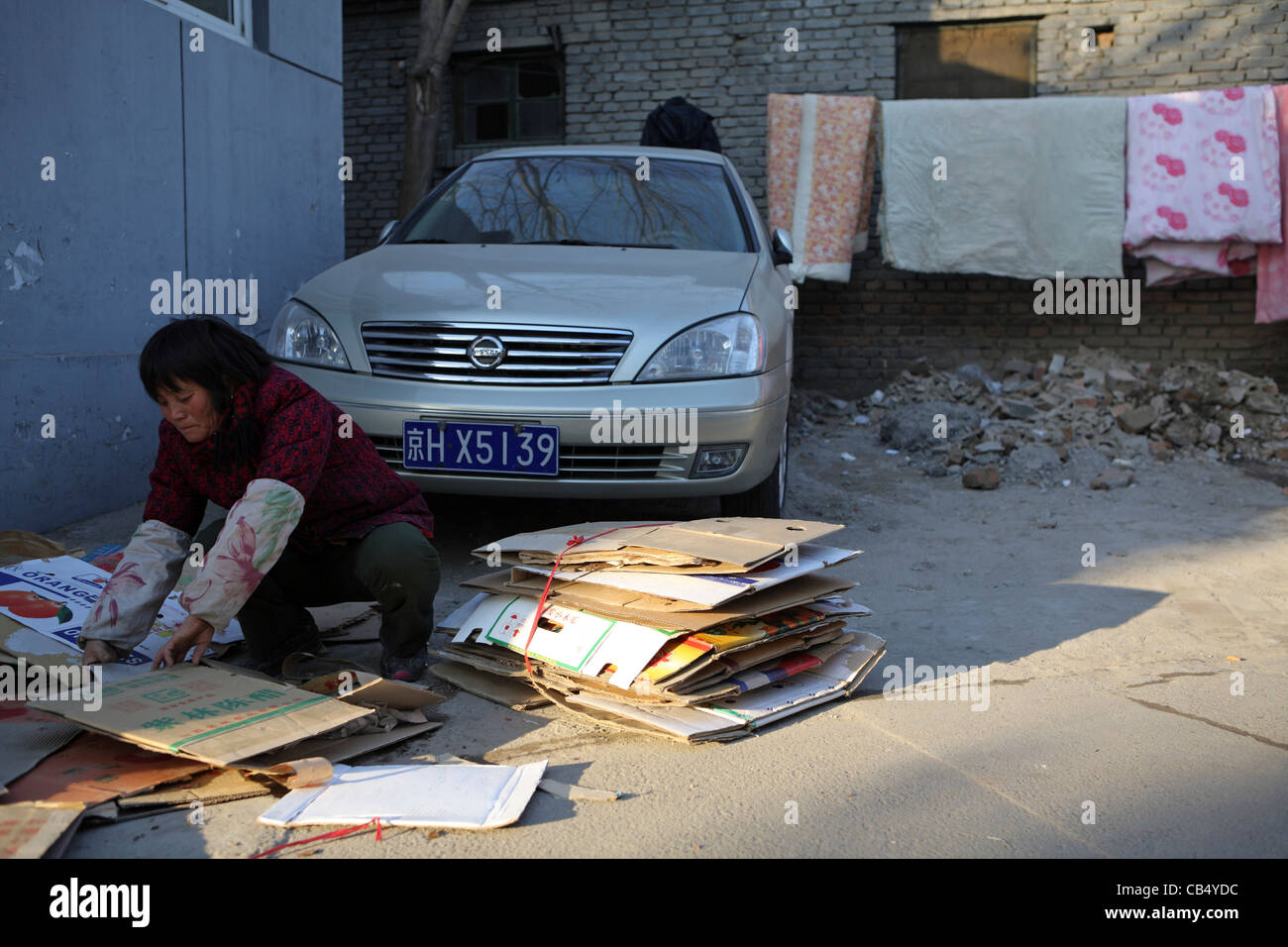 Chinesische Migrantin Gegenüberstellung mit gesammelten wiederverwertbare Karte vor modernen teuer importiertes Auto, Peking, China Stockfoto