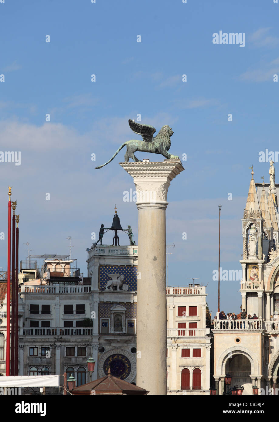 Der geflügelte Löwe von San Marco auf seiner Säule in San Marco Square mit den berühmten Uhrturm mit zwei Mauren dahinter Stockfoto