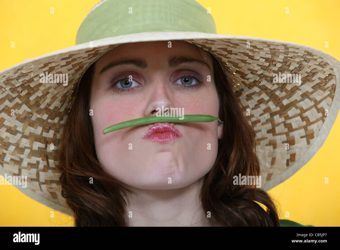 Frau eine grüne Bohnen zwischen ihre Lippen und Nase balancieren Stockfoto