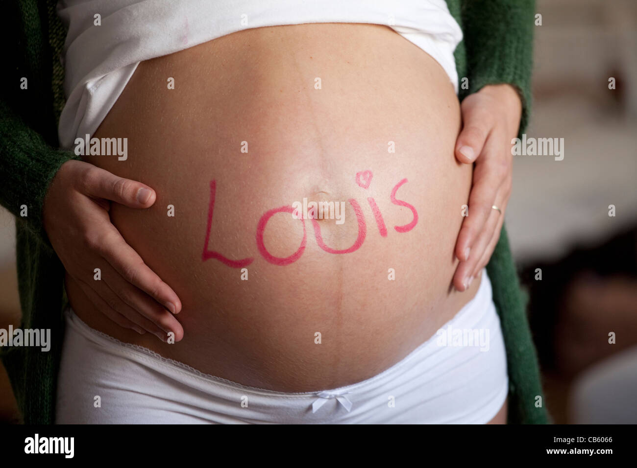 Hautnah auf dem Bauch einer schwangeren Frau mit dem Namen Louis darauf geschrieben. Stockfoto