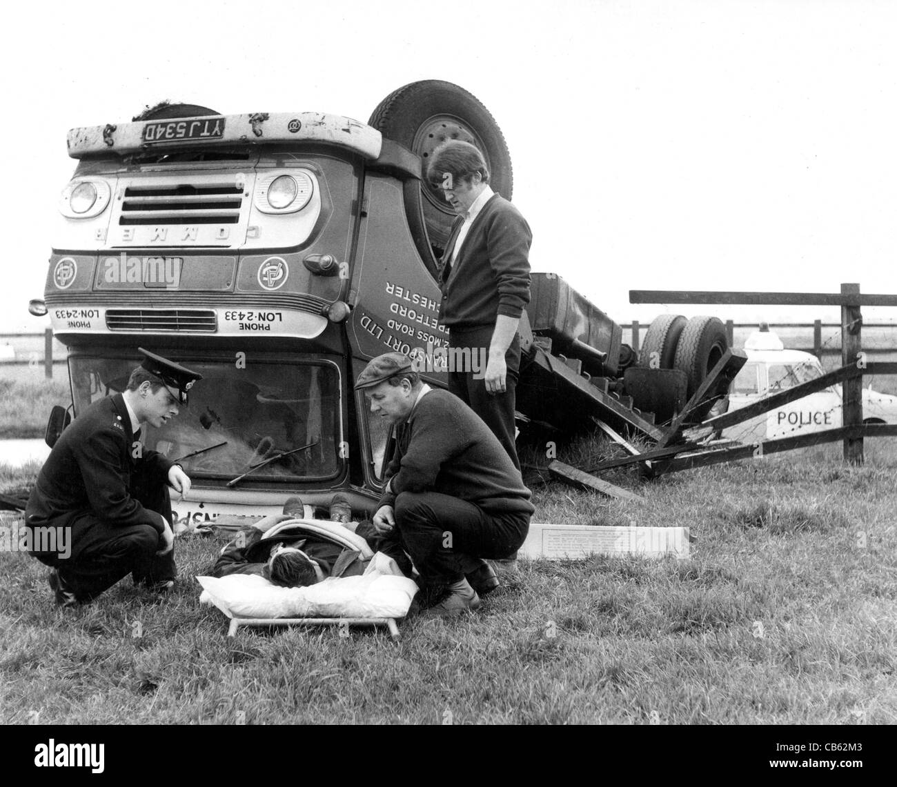 Ein Polizist und zwei Männer trösten einen verletzten Fahrer vor seinem umgekippten LKW im BILD VON DAVID BAGNALL 1967 Stockfoto