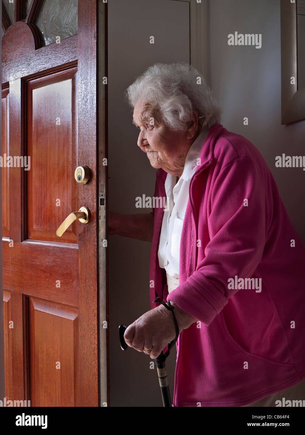 Ältere Dame ÖFFNEN TÜR WARTEN Nachdenklich besorgt, 98 Jahre ältere Frau mit Stock auf Ihre offene Tür warten Stockfoto