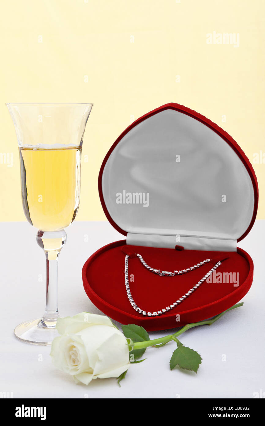 Foto von einer Diamant-Halskette in ein Herz geformt Schmuckschatulle mit einem Glas Champagner und weiße rose. Stockfoto