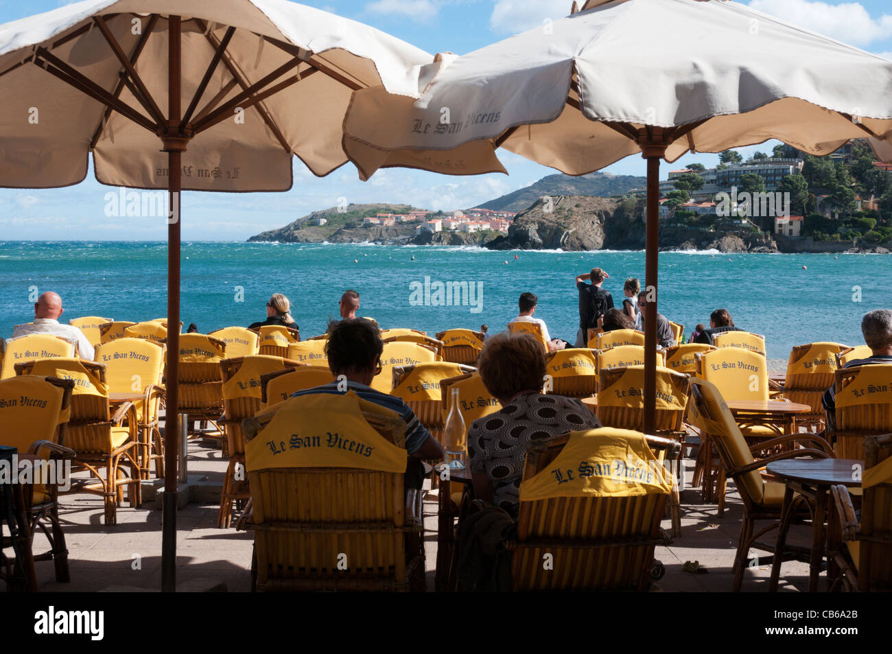 Touristen sitzen und entspannen unter Sonnenschirmen am Strandcafé in Collioure, Südfrankreich Stockfoto