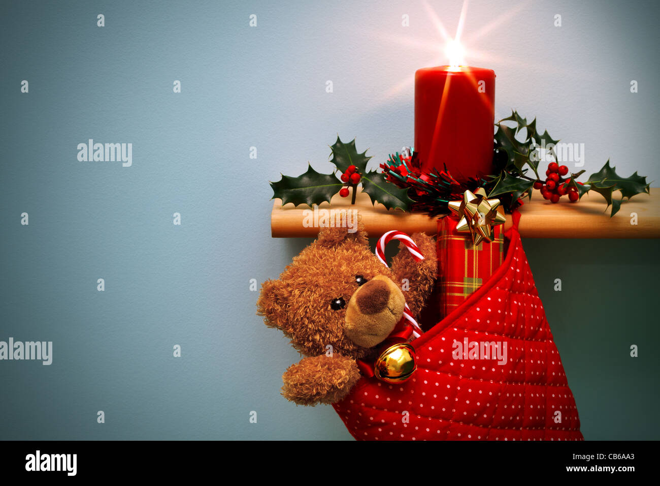Foto von einem Weihnachts-Strumpf voller Geschenke und eine Kerze, umgeben von holly Stockfoto