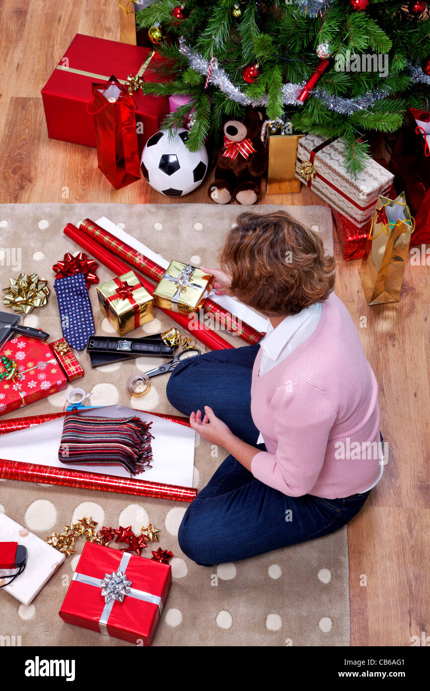 Obenliegende Foto einer Frau saß auf einem Teppich zu Hause verpacken ihre Weihnachtsgeschenke. Der Teddy ist generisch und ist keine Marke Bär. Stockfoto