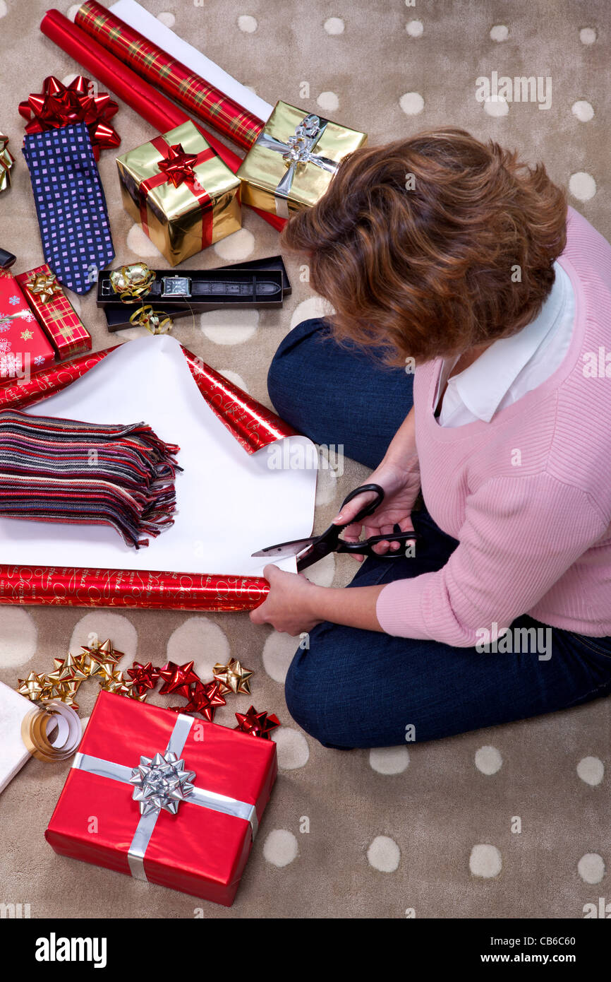 Foto einer Frau saß auf einem Teppich zu Hause Umhüllung einen Schal für ein Weihnachtsgeschenk. Stockfoto
