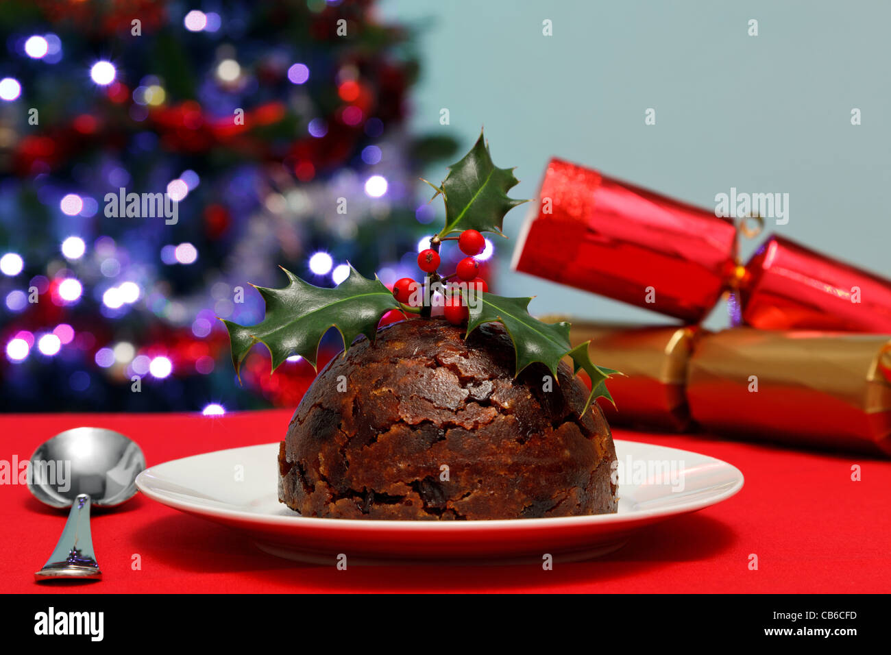 Foto von einer Christmas Pudding mit Holly an der Spitze mit Baum und Cracker im Hintergrund. Stockfoto