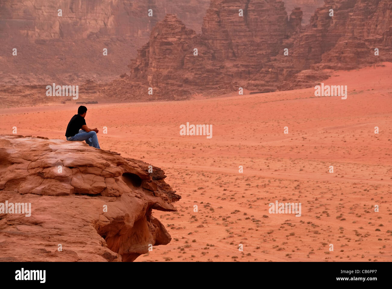 Ein Mann sitzt auf Wüste einer Klippe und genießen den Blick auf das Wadi Rum in der warmen Luft der Wüste. Stockfoto