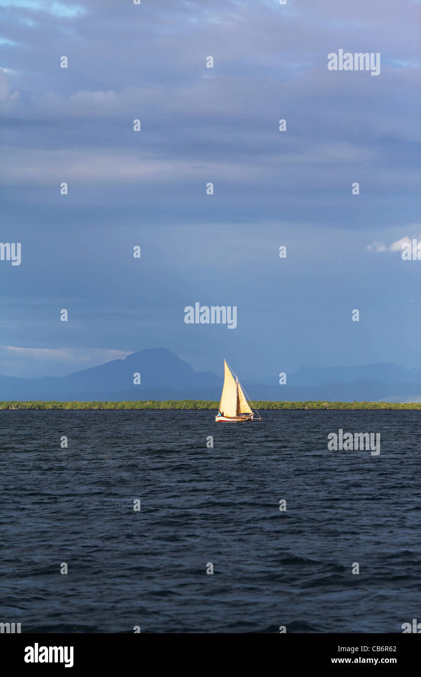 Ein traditionelles madagassischen Boot oder Boote, Segeln mit vollen Segeln bei Sonnenuntergang vor Ankify, Madagaskar. Berge und Mangroven. Stockfoto