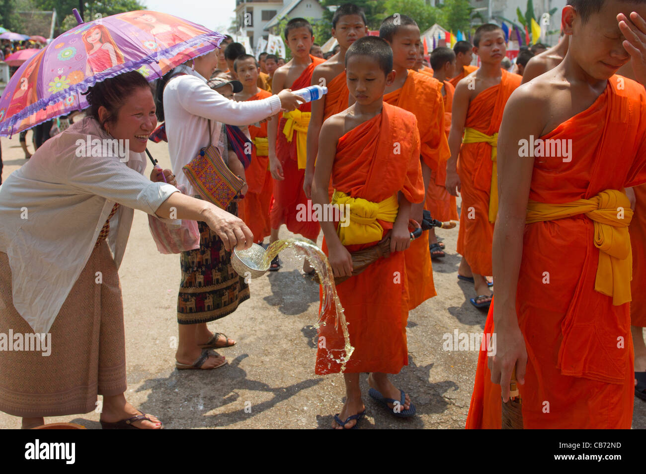 Buddhistische Mönche in einer Prozession mit Wasser für einen Segen auf sie geworfen von einer lächelnden Lao Frau auf Mue Nau, den mittlere Tag der Lao Neujahr (Pi Mai Lao), Luang Prabang, Laos Stockfoto