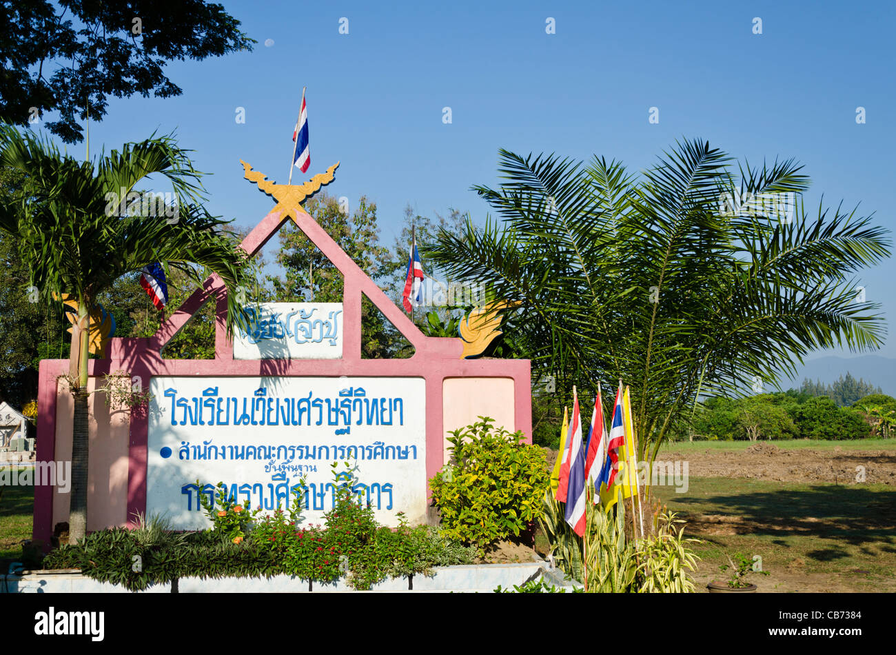 Aufwendig verziert rosa Schild mit Chofa & Thai Fahnen für die Grundschule in Saraphi in Nordthailand Stockfoto
