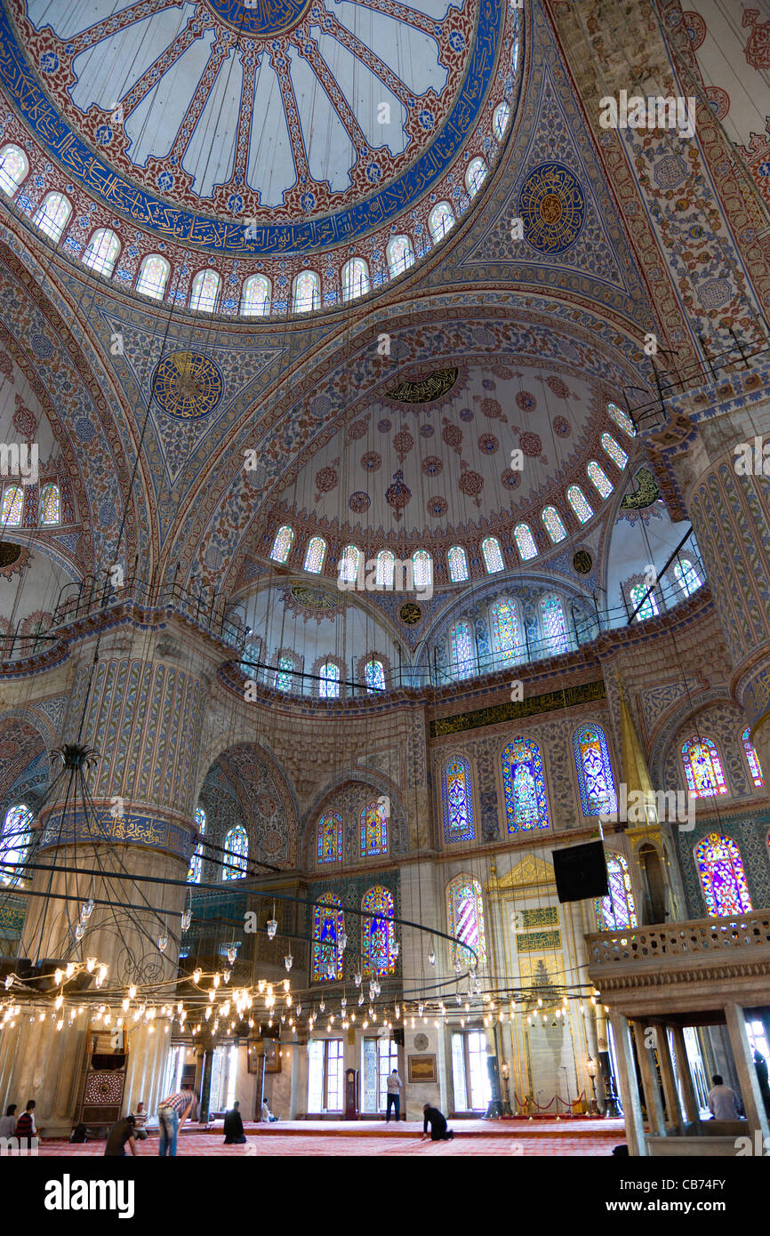 Türkei, Istanbul, Sultanahmet Camii, die blaue Moschee-Interieur mit Menschen beim Gebet unter Kronleuchtern und verzierten Kuppeln. Stockfoto