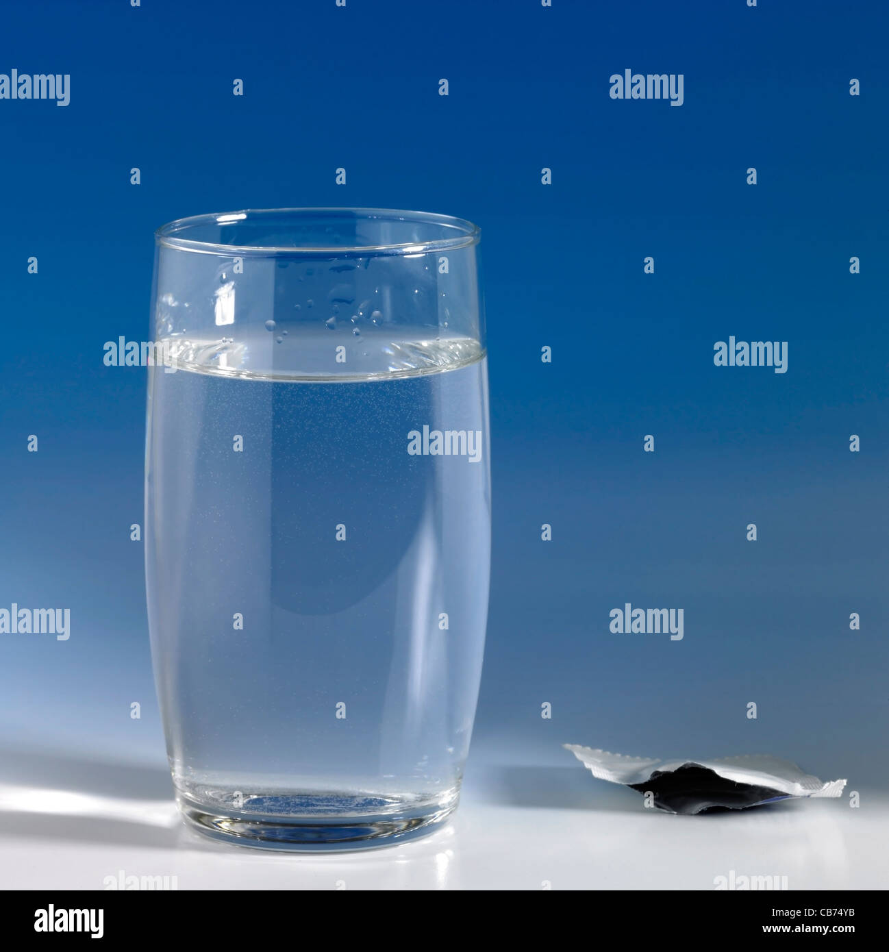 Fizzy Tablette in einem Glas Wasser, das leere Gehäuse neben gelöst. Studio in blauen Rücken geschossen Stockfoto