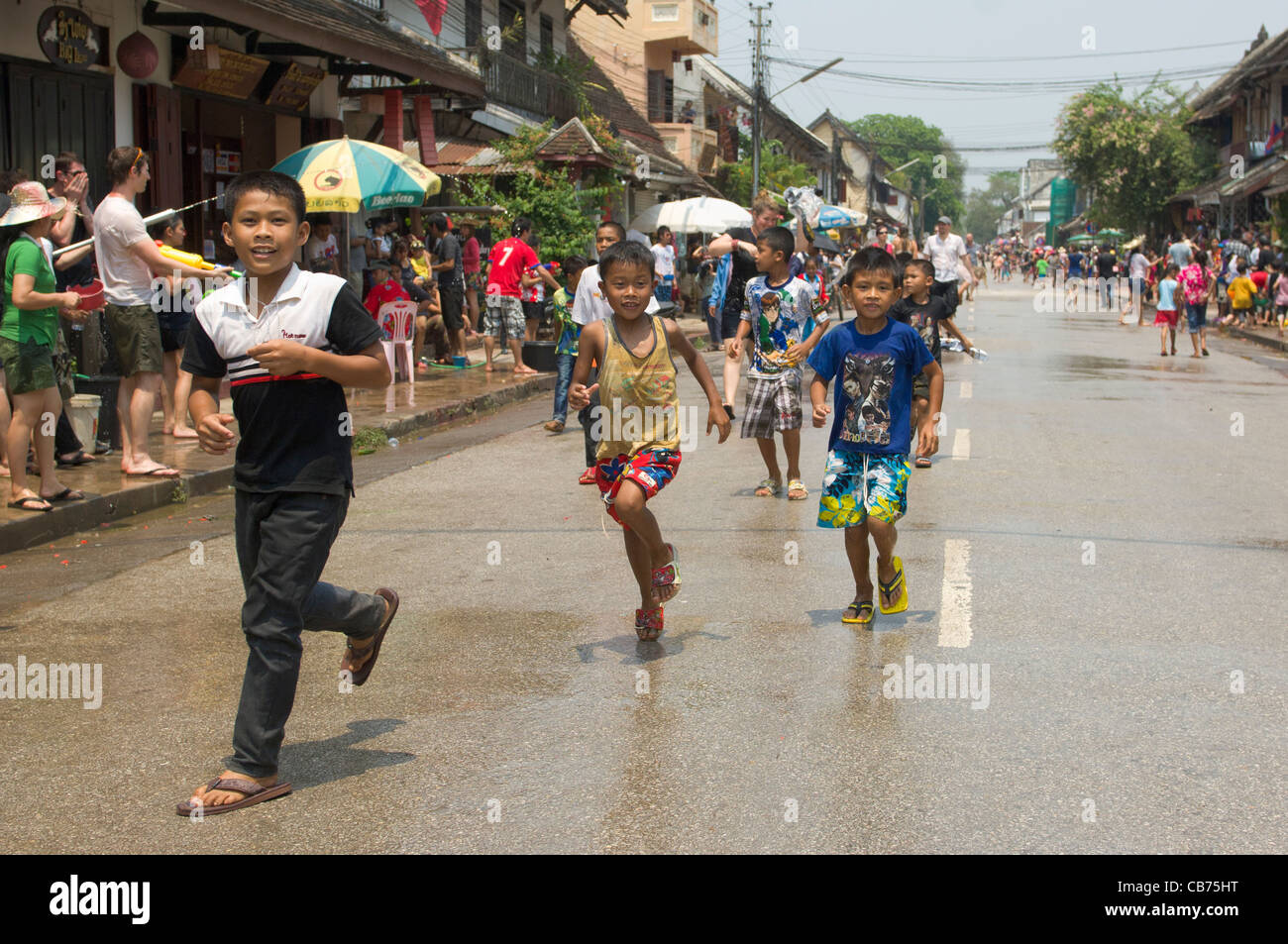 Kleine Jungen läuft entlang der Hauptstraße vor der Prozession auf Mue Nau, Lao Neujahr (Pi Mai Lao), Luang Prabang, Laos Stockfoto