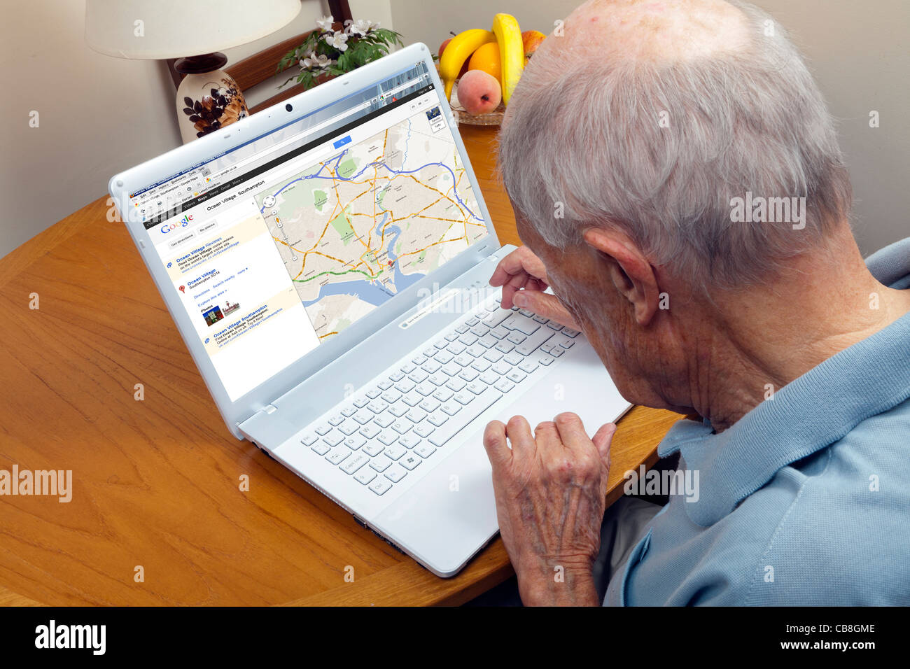 Älterer Herr, der das Surfen im Internet auf der Suche nach Wegbeschreibungen und Karten auf einem Laptop Stockfoto